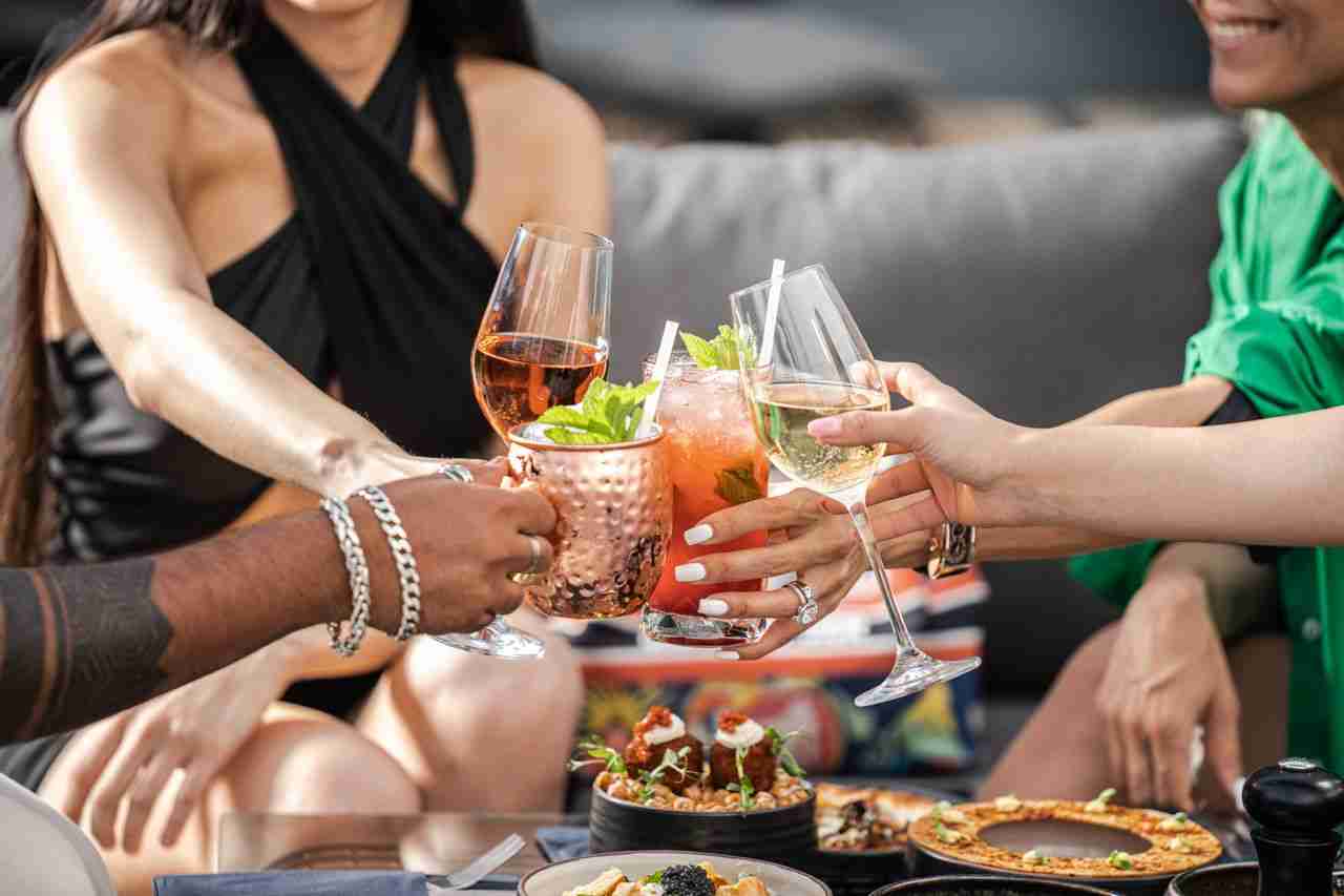 ours-journey Group of friends clinking glasses with cocktails at an outdoor terrace party in Dubai.