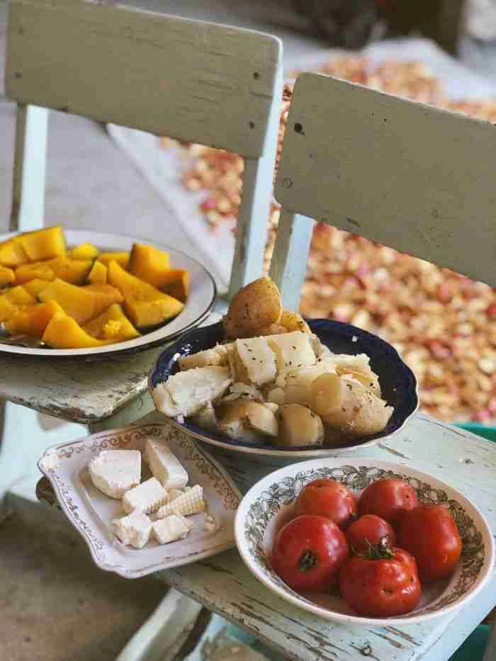 gallery-2 Warm rustic scene featuring potatoes, pumpkin, cheese, and tomatoes arranged on vintage plates.
